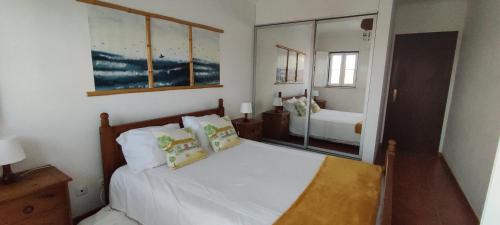 a bedroom with a bed with white sheets and a mirror at Casa com Cor in Zambujeira do Mar
