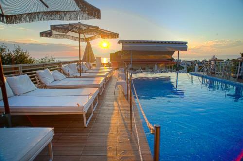 a hotel swimming pool with white beds and umbrellas at Anny Residences & Suites in Skala Kallirachis