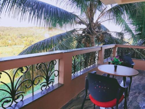 d'un balcon avec une table, des chaises et un palmier. dans l'établissement The Narrow Way Edward Guest House, à Candolim