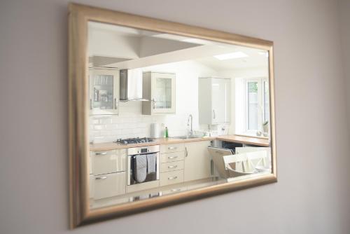 a mirror reflecting a kitchen with white cabinets at Knollmead House in Surbiton