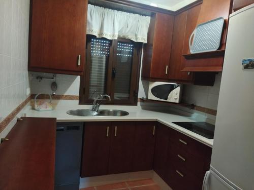 Una cocina con armarios de madera, fregadero y microondas. en Casa Rural Alamillo, en Luque
