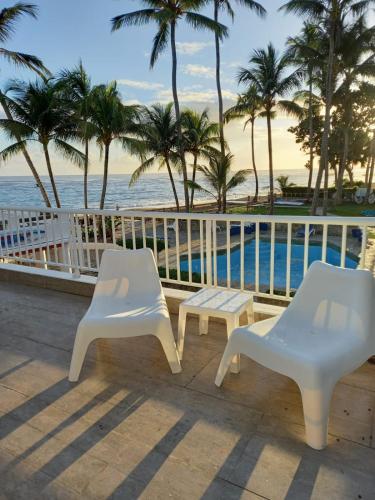 two white chairs and a bench next to the ocean at Cabarete Kite Beach Rooms & Condos in Cabarete