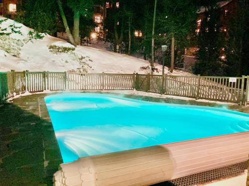 une grande piscine bleue avec clôture et neige dans l'établissement Appartement ARC 1950 m, Ski au pied, piscine extérieure chauffée, remontées mécaniques à 100m, sauna et salle de sports, à Arc 1950