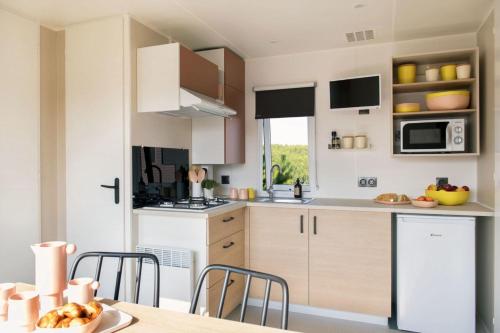 a kitchen with white cabinets and a table with chairs at Camping La Baie des Voiles in Porto-Vecchio
