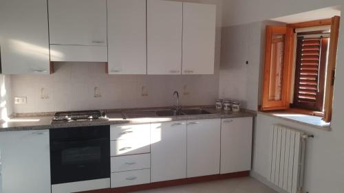 cocina con armarios blancos, fregadero y ventana en Appartamento "Al Borgo Antico", en Aieta