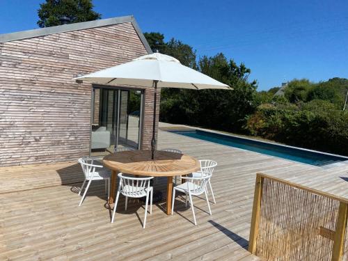 una mesa de madera y sillas con una sombrilla en la terraza en Magnifique villa avec piscine, à 5 min des plages en Landunvez