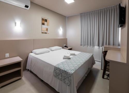a bedroom with a bed and a desk and a window at Hotel Pitol in Balneário Camboriú