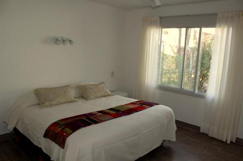 1 dormitorio con 1 cama blanca grande y ventana en Casita en Chacras en Luján de Cuyo