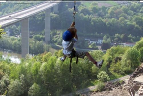 a person on a zip line over a bridge at Lesse en Ciel vous accueille avec plaisir . in Houyet