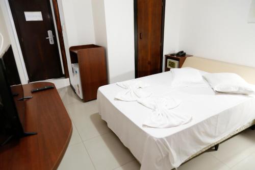 um quarto com uma cama com lençóis brancos e uma televisão em Hotel Suiça Faber em Balneário Camboriú