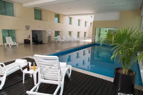 a pool with white chairs and a palm tree in a building at Fiesta Inn Ecatepec in Mexico City