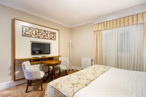 a bedroom with a bed and a desk and a tv at Pousada Italia Eleganza in Campos do Jordão