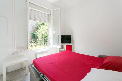 Ce lit rouge se trouve dans une chambre blanche dotée d'une fenêtre. dans l'établissement Charming Parisian studio!, à Paris