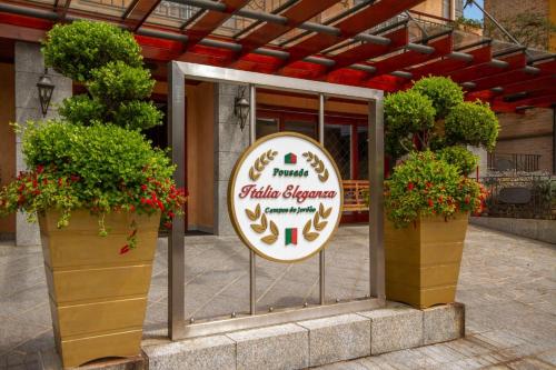 a sign in front of a building with two potted plants at Pousada Italia Eleganza in Campos do Jordão