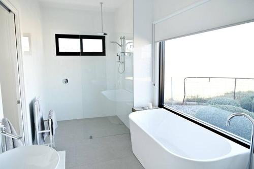 baño blanco con bañera grande y ventana en Luxury Modern Farm Stay Home in Southern Highlands en Joadja Creek