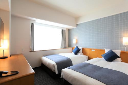 a hotel room with two beds and a desk and a window at HOTEL MYSTAYS Okayama in Okayama