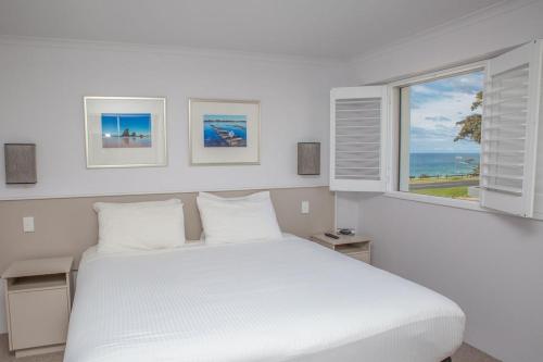 a white bedroom with a white bed and a window at Amooran Oceanside Apartments and Motel in Narooma