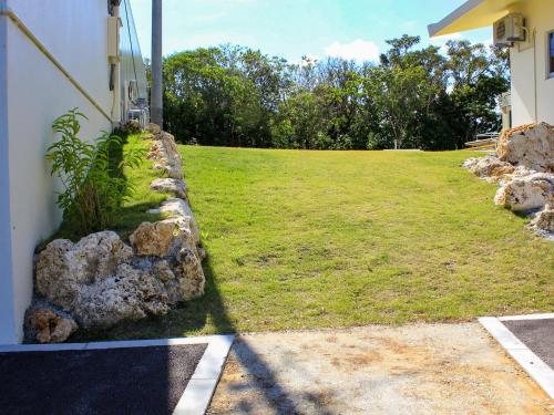 a grassy yard with a rock wall next to a house at ペンション村山里 in Yamazatu