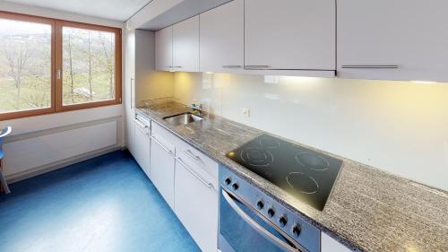 a kitchen with white cabinets and a sink and a stove at Reka-Feriendorf Disentis in Disentis