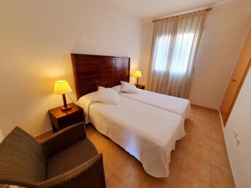 a bedroom with a large white bed and a chair at Apartamentos Las Dunas-B in Riumar