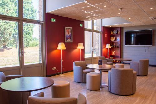 una sala de estar con mesas y sillas y TV de pantalla plana. en Campanile Dunkerque Sud - Loon Plage, en Loon-Plage