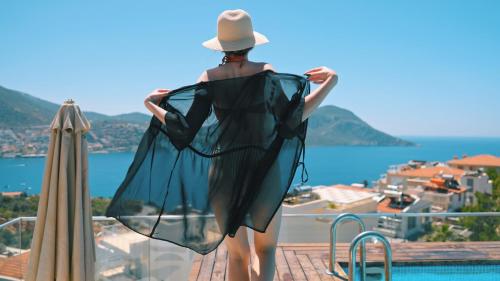 a woman in a black dress and hat standing on a balcony overlooking the ocean at Rhapsody Hotel & Spa Kalkan in Kalkan