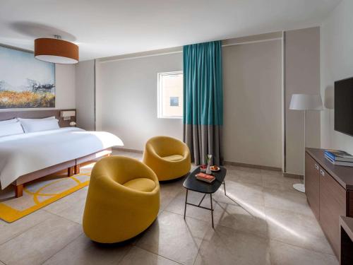 a hotel room with a bed and two yellow chairs at Adagio Aparthotel Jeddah Malik Road in Jeddah