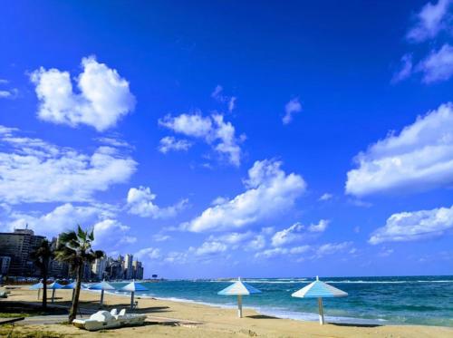 a beach with umbrellas and the ocean with buildings at شقة فندقية مكيفة ميامي ع البحر مباشرةً in Alexandria