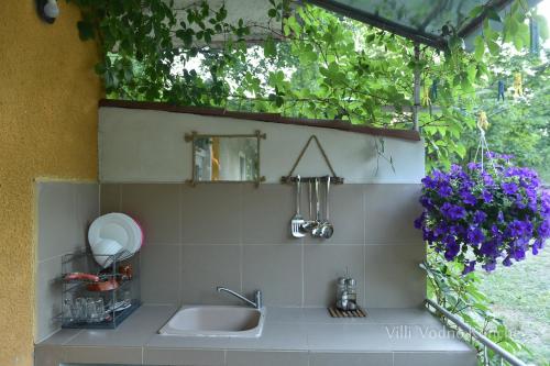 um balcão de cozinha com um lavatório e flores roxas em Вили Водно Конче Villas Vodno Konche em Ahtopol