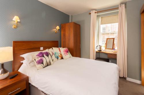 a bedroom with a white bed and a desk and a window at Queens Head Hotel in Berwick-Upon-Tweed