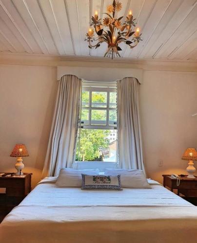 a bedroom with a bed with a chandelier and a window at Pousada Vila Brasil in Petrópolis