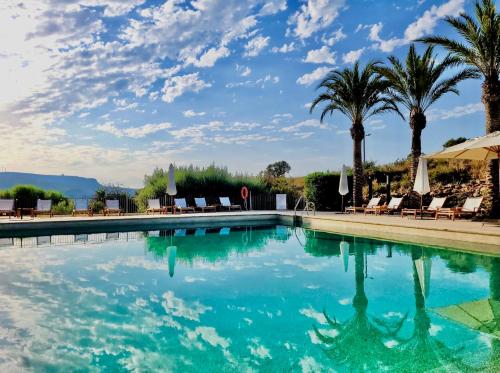 a swimming pool with palm trees and chairs at Real Agua Amarga La Joya - Adults Only in Agua Amarga