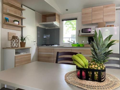 a kitchen with a table with a bowl of bananas and a pineapple at MOBIL HOME Climatisé G058 in Aureilhan