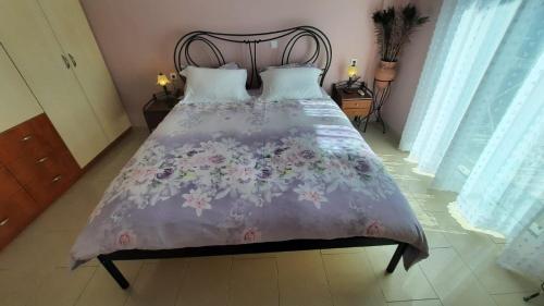 a bed with a purple comforter with flowers on it at IOANNIS - Room with balcony near Limnopula in Gavrolímni