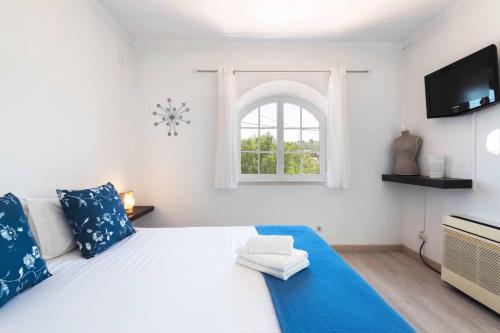 a bedroom with a white bed with blue pillows and a window at Sesimbra Stylish Villa by Homing in Sesimbra