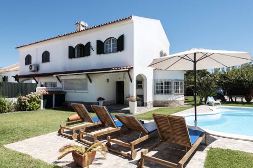a patio with chairs and an umbrella next to a pool at Sesimbra Stylish Villa by Homing in Sesimbra