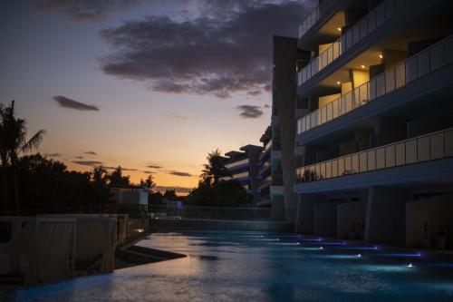 an empty swimming pool in front of a building at sunset at Palmaïa The House of AïA All Inclusive Wellness Resort in Playa del Carmen