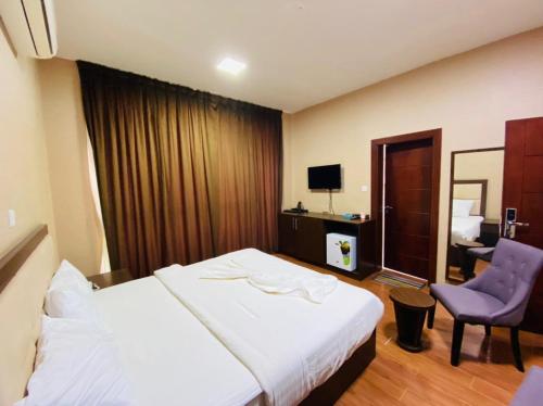 a hotel room with a white bed and a purple chair at Alpha Suites Hotel in Salalah
