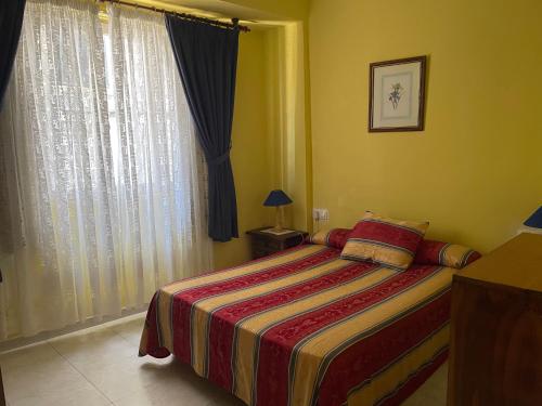 a bedroom with a bed with a striped blanket and a window at Apartamento economico a 100m de la playa ESTANCIA MINIMA 4 NOCHES in A Pobra do Caramiñal