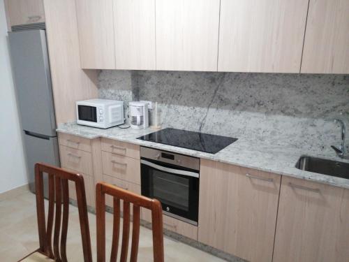 a kitchen with a sink and a microwave and two chairs at Apartamento Costa Riazor Coruña in A Coruña