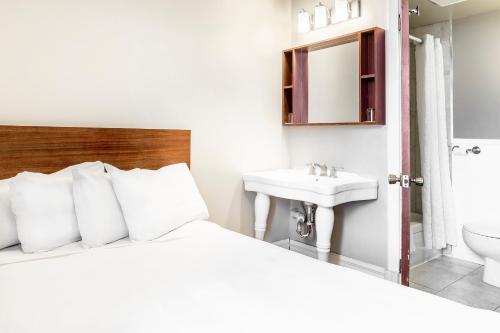 a white bedroom with a bed and a sink at Hotel Ermitage in Quebec City
