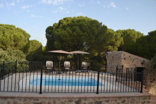 a pool with umbrellas and chairs and a fence at Alojamiento Rural Dehesa La Estancia in Andújar