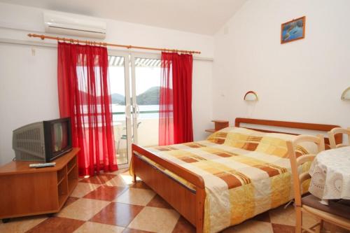 a bedroom with a bed and a tv and red curtains at Apartments by the sea Pasadur, Lastovo - 8391 in Lastovo