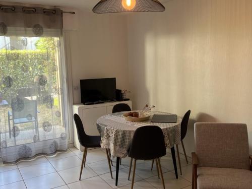 une salle à manger avec une table, des chaises et une télévision dans l'établissement Appartement T2 avec Jardin, Proche Plage et Centre, Parking Privé, Animaux Acceptés, Wi-Fi Gratuit - FR-1-487-342, à Cabourg