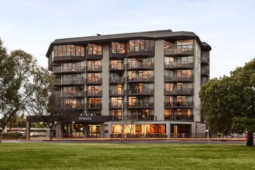 a large building with many windows and a grass field at Rydges South Park Adelaide in Adelaide