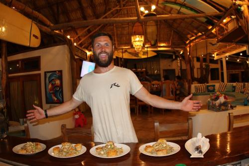 Un uomo in piedi davanti a un tavolo con piatti di cibo di Sirena Surf Lodge Miramar Nicaragua a Miramar