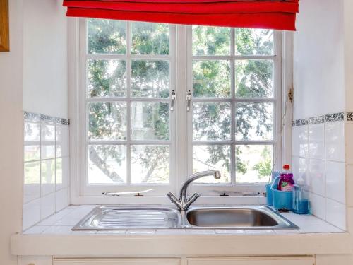 a kitchen sink with a window with a red curtain at Sea View in Penzance