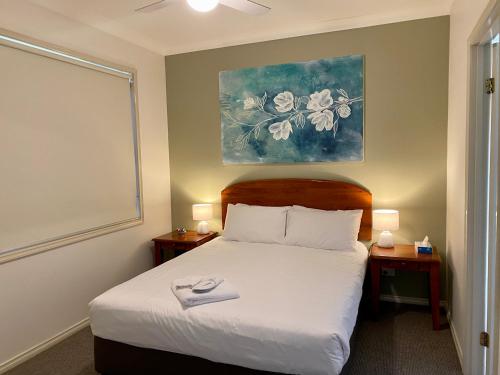 a bedroom with a white bed with a painting on the wall at Beautiful Villa in the heart of the Hunter Valley in Pokolbin