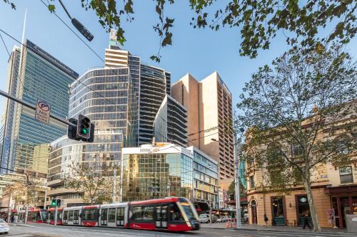 eine Stadtstraße mit einem Bus vor hohen Gebäuden in der Unterkunft Meriton Suites Campbell Street, Sydney in Sydney