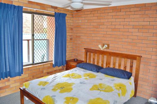 a bedroom with a bed with blue curtains and a brick wall at Cameo Court 2 in South West Rocks